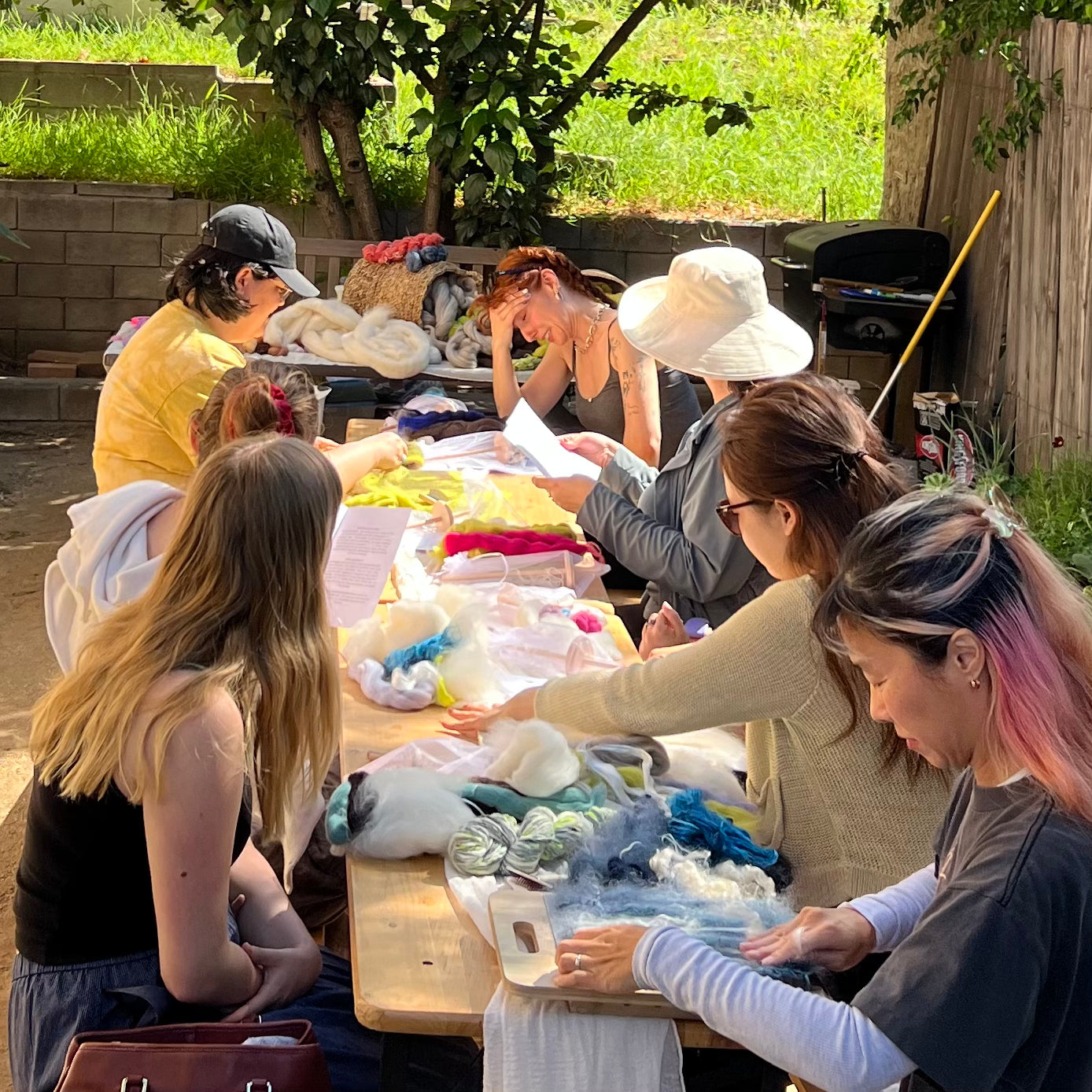 Group of people working on craft projects outdoors at a table.